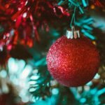 Close-up of a glittery red Christmas ball hanging on a green tree branch.